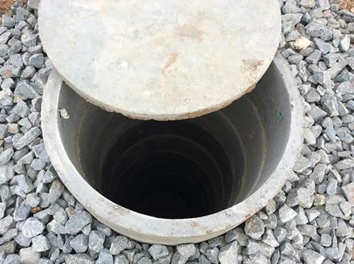 Concrete ring well with its lid, set in a bed of blue metal