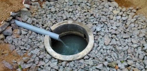 Rainwater flowing from a pipe into a concrete-ring recharge well surrounded by gravel