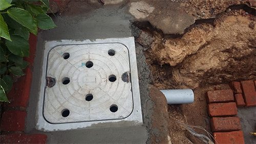 Perforated cover fitted at a garden edge next to a PVC pipe