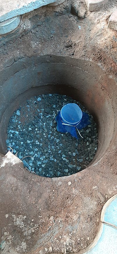 Ring well lined with blue metal stones and a mesh-wrapped inlet